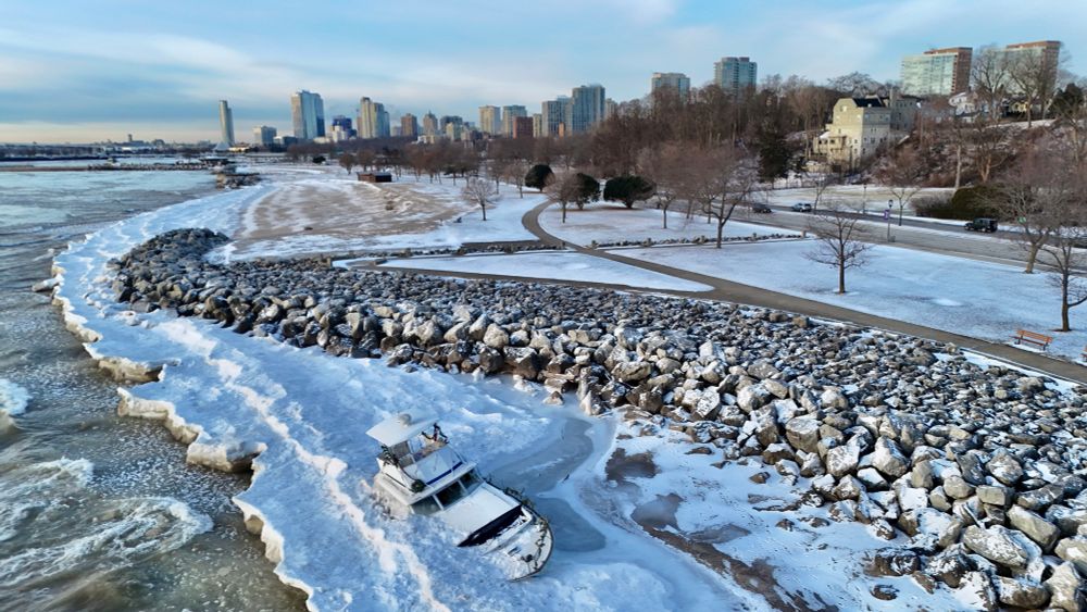 A boat frozen into the ice on a rocky shore with a city in the background