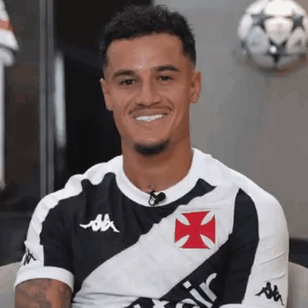 a soccer player is smiling while wearing a black and white shirt with a cross on it .