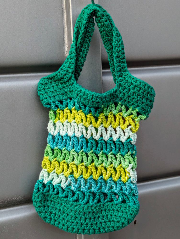 A mini crochet market bag that is green, turquoise, yellow, and white.