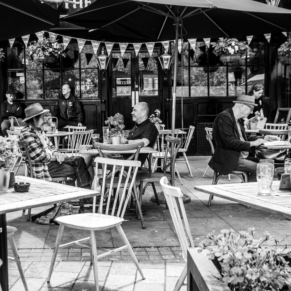 3 men at separate tables outside a cafe two with hats. Black and white photo 