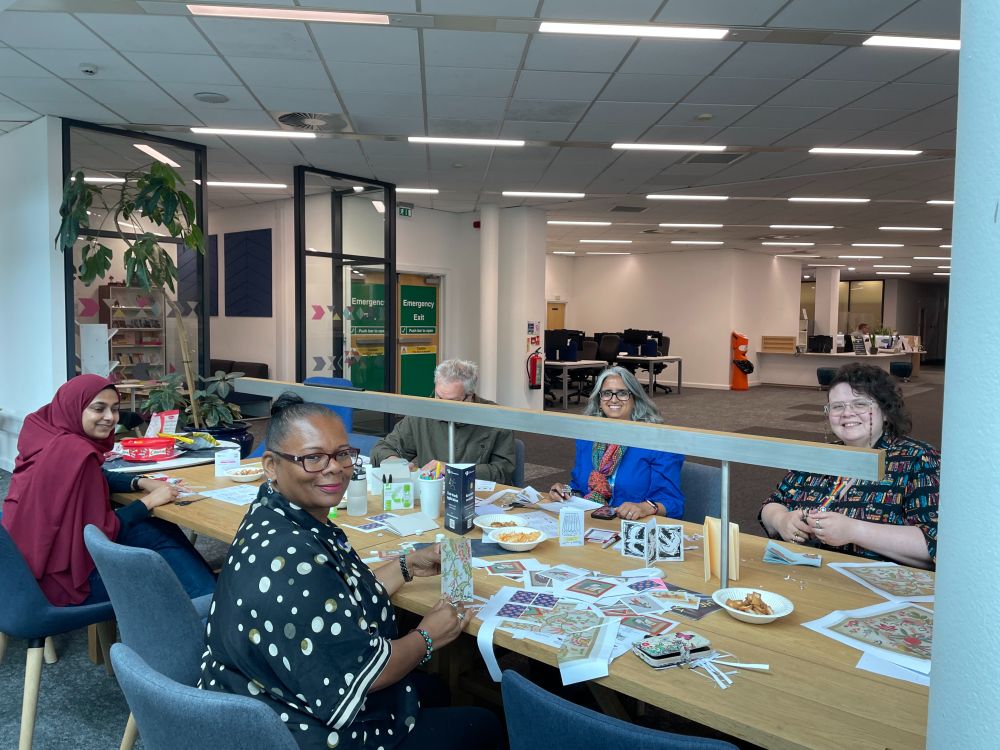 A photo of 5 people sat around a table with craft supplies on making zines.