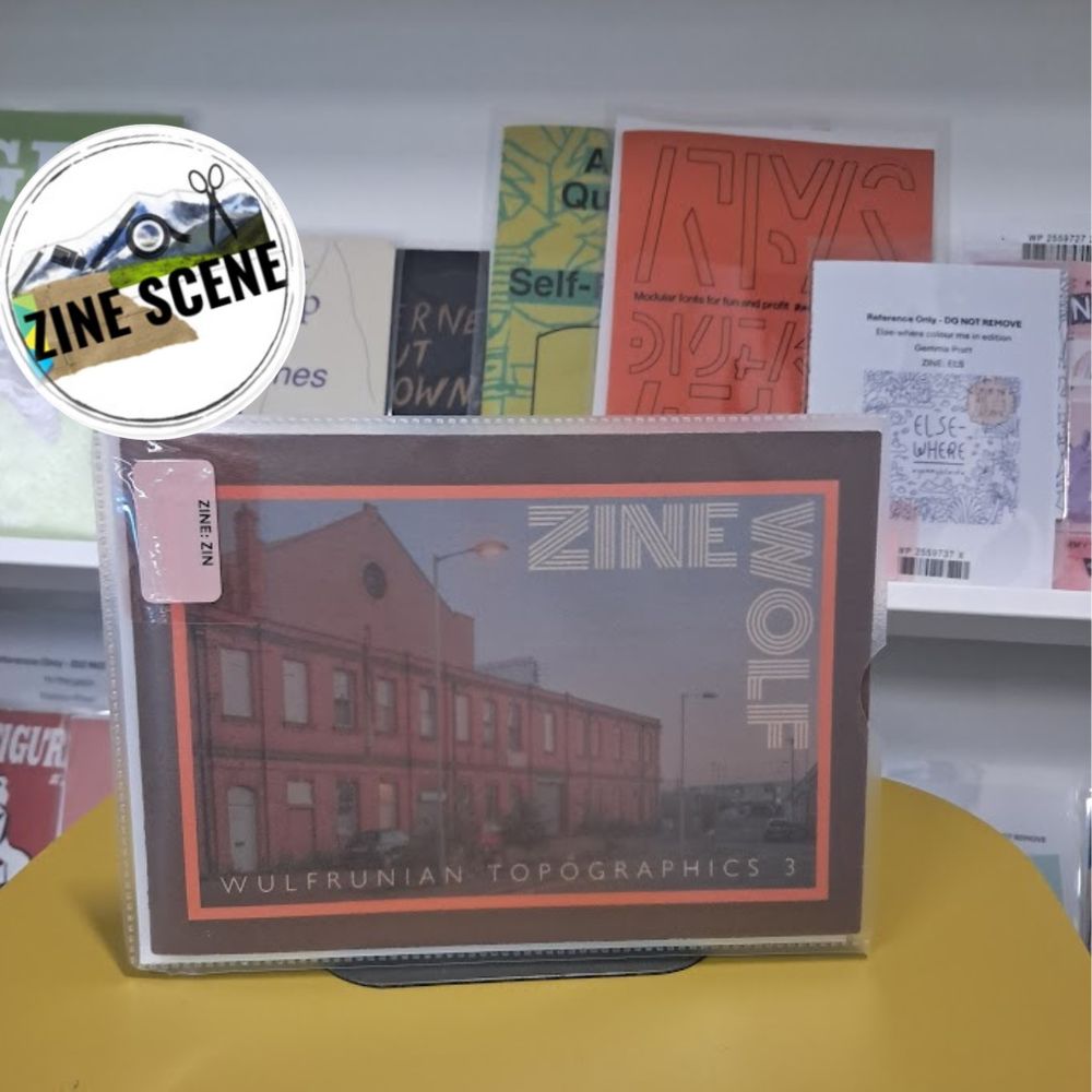 A zine called Zine Wolf: Wulfrunian Topographics 3 on a table in front of our zine shelves. The Zine Scene sticker is in the top left corner.