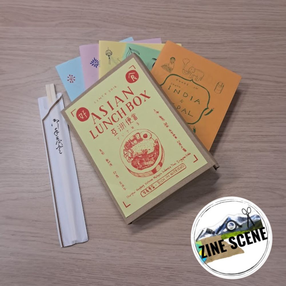 A photo of a box set of zines called Asian Lunch Box with 5 zines peeking out of the box, including one called India and Nepal, with some chopsticks on the side.
