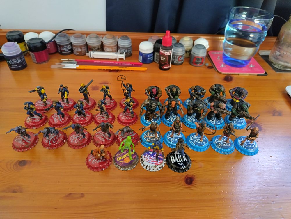 A collection of minis on my desk. The left half are in red Nuka Cola bottle caps as their bases while the ones on the right are on blue Nuka Cola bottle caps.

I made some Vault vault Dwellers, rad ghouls, a Glowing One, Super Mutants, regular mutants, a mysterious stranger, an escaped convict in orange jumpsuit and a AWI guy too

Paint pots, brushes and a glass of water lurk in the background. Stay hydrated kids 👍