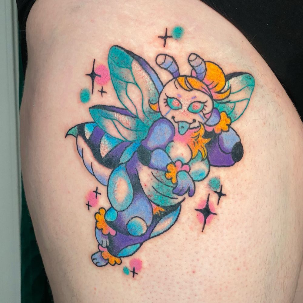 A tattoo on my clients upper right thigh of her fursona Missie. She is a blue bee with fluffy yellow fur around her wrists, ankles, and neck. She wears her hair in a bun on the top of her head and is sticking out her pierced tongue teasingly. Shes surrounded by teal and pink sparkles. 