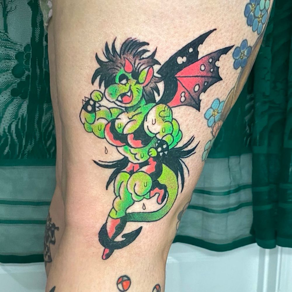 A tattoo on the side of my clients knee of a green dragon girl flexing her bicep. Shes super muscular and sweaty with a long 80s style mullet. 
