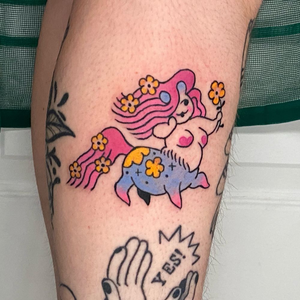 A tattoo on my clients outer right ankle of a centaur girl. She has flowing pink hair and a long pink tail. Botb decorated by yellow flowers. She has a chubby, stout little body. The horse half being blue with yellow flowers decorating patters and little pink feet. Shes blushing while holding a yellow flower and smiling. Her nipples are cute pink hearts. 


##qttr #queertattooartist #southernqttr#contemporarytattoo #transtattooartist #virginiatattooers #rvatattooer #richmondtattooartist 
