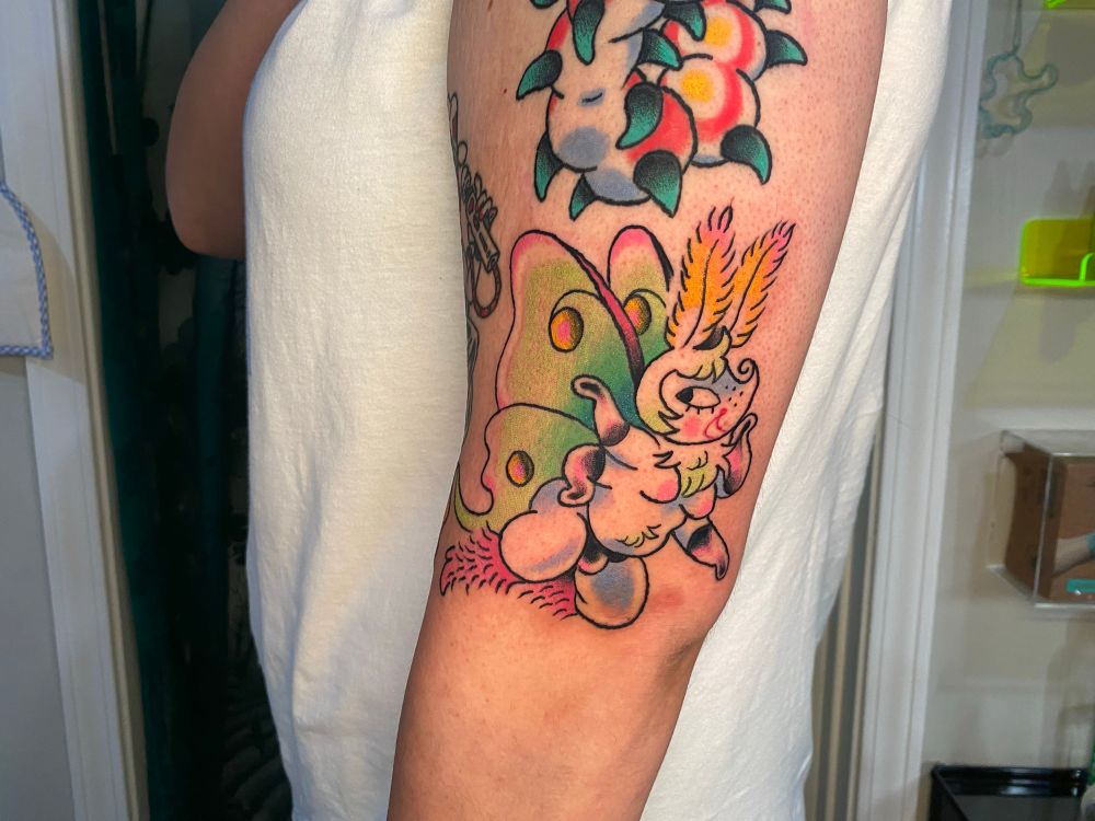 A tattoo on my client’s left outer arm right next to her elbow of an anthro luna moth with shiny latex gloves, panties, and fuzzy pink boots 