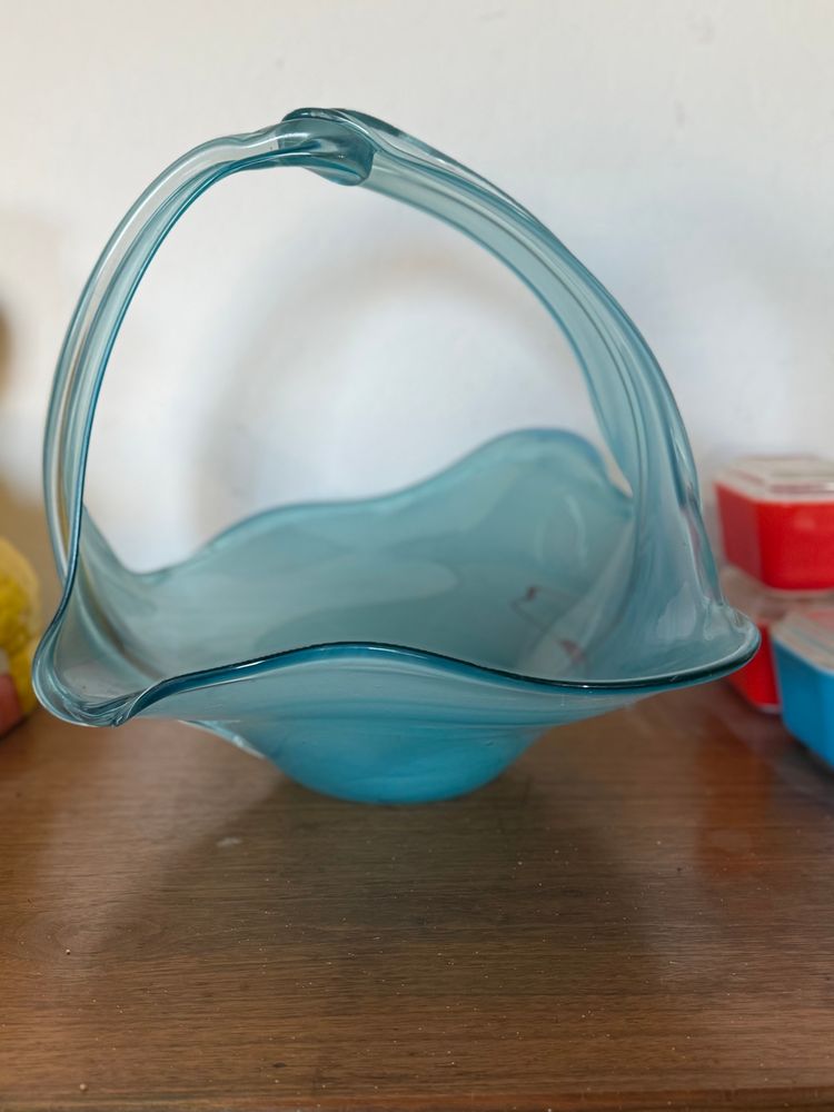 Side view of a blue glass basket on a sideboard with a small assortment of colorful Pyrex refrigerator dishes.