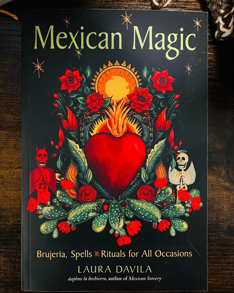 The cover of Mexican Magic: Brujería, Spells & Rituals for All Occasions by Laura Davila. The design features a fiery red sacred heart surrounded by blooming red roses, green prickly pear cacti, and a radiant golden sun. To the left, a red skeletal figure stands, while to the right, a white skeleton with angel wings and a halo appears. The background is deep black, with small glowing stars scattered throughout. The book’s title is in large green letters at the top, with the subtitle and author's name in gold at the bottom. The cover blends traditional Mexican folk magic imagery with vibrant, mystical symbolism.