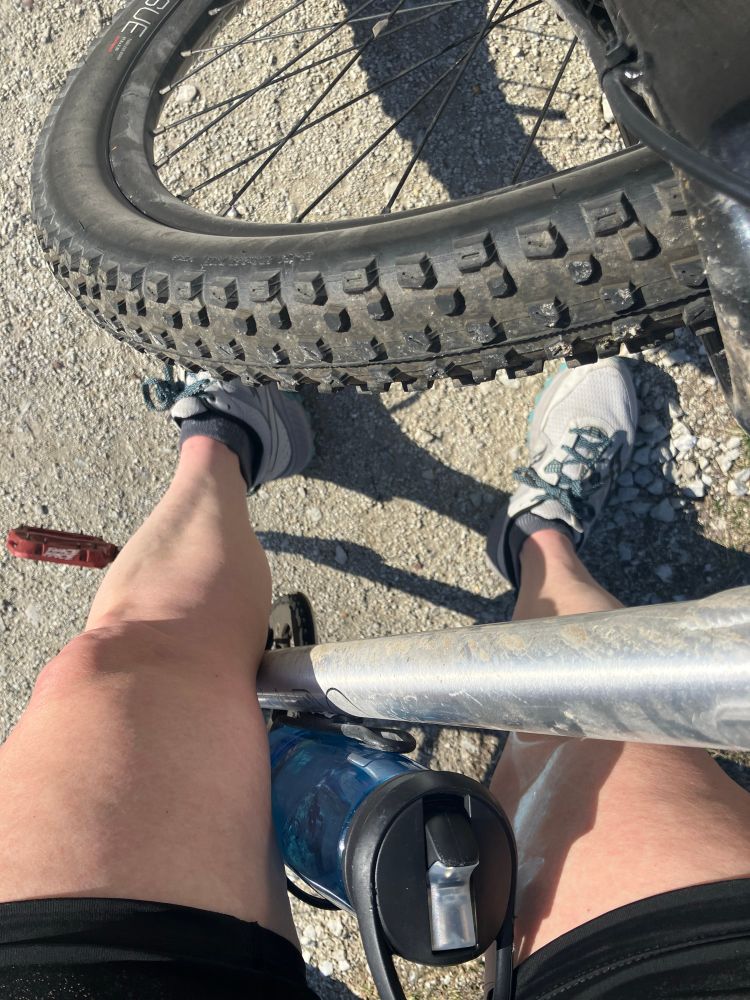 Picture of legs and bike on a rock trail with the sun shinning.