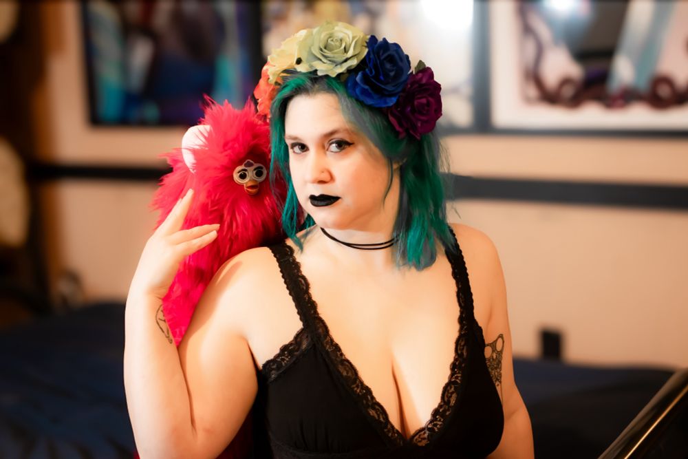 A photo of Embyr wearing a flower crown and posing with a bright pink long furby abomination 