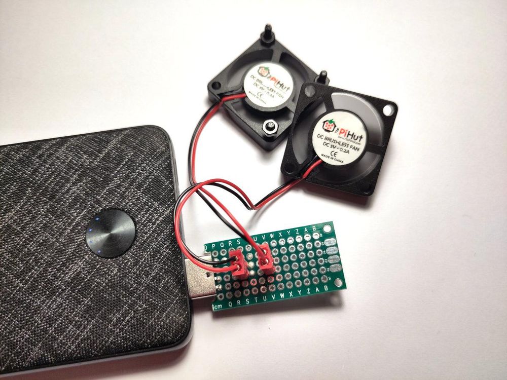 A powerbank powering two small 5V fan via a DIY adapter made from a USB connector and a prototype board.