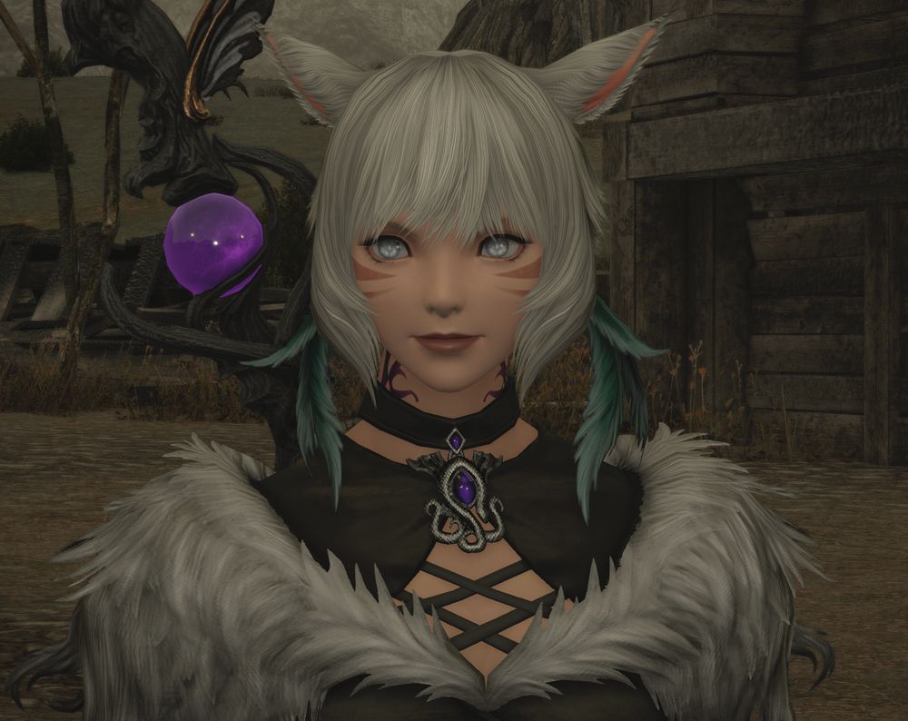 FFXIV screenshot depicting Y'shtola's first appearance in the Shadowbringers expansions.

She wears black robes adorned with silver fur. She has white hair with green feathers tied into it. Her eyes are milky white from blindness. She carries a staff with a purple orb.