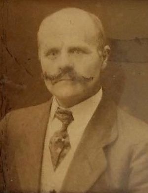 A scan of an old amber and white photo of Thortveit. He is in a suit and tie with a vest. A balding man, he has a magnificent mustache that tries to hide an unsmiling mouth. 