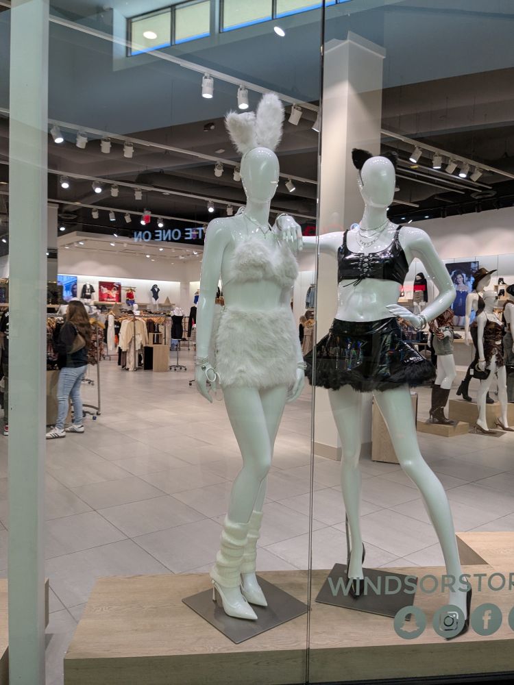 Two mannequins. The one on the left has a white fluffy bunny outfit and the one on the right has a sleek black cat outfit. Both sexy
