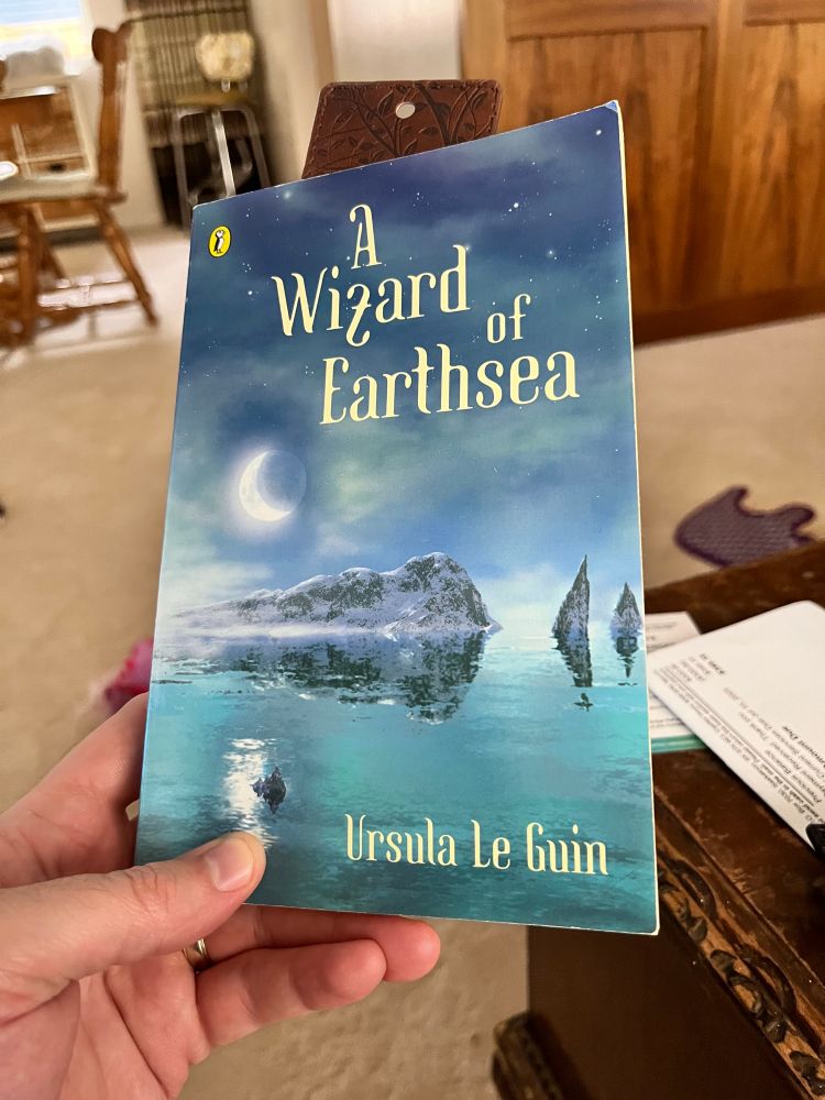 A hand holding “A Wizard of Earthsea” by Ursula Le Gin.