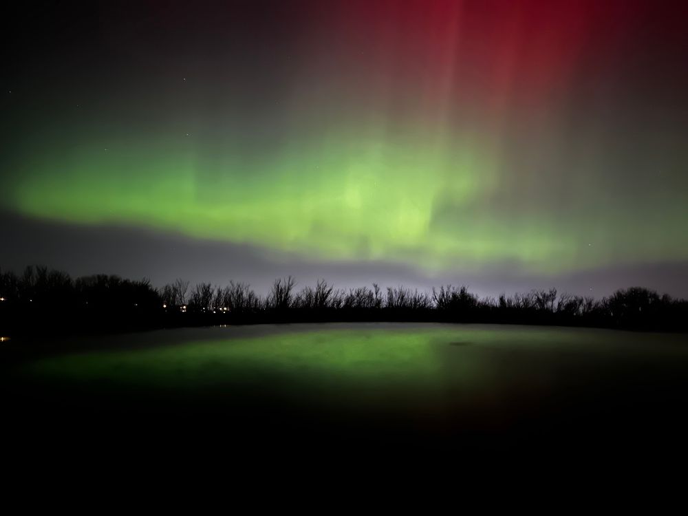 Green northern lights. A reflective surface is near the bottom of the frame and the lights can be seen in the reflection as well