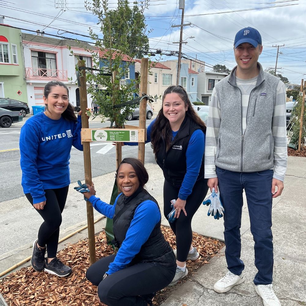 Four smiling volunteers stand by a newly planted street tree.