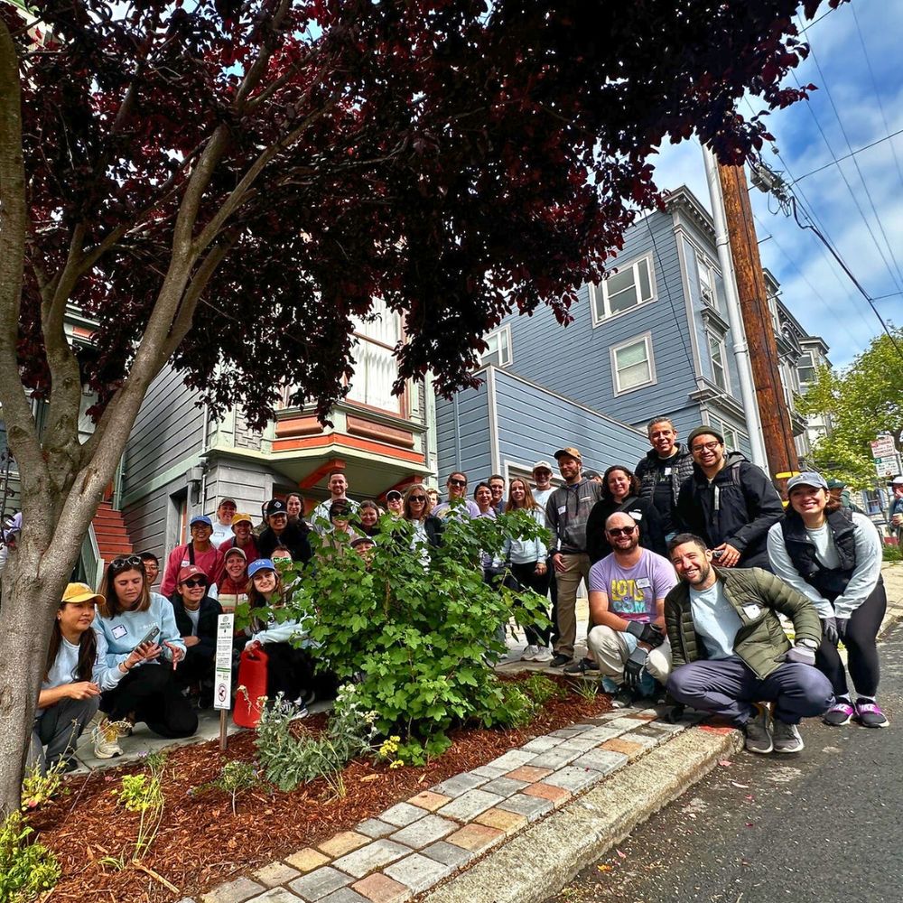 Group photo of 30+ volunteers and staff by a sidewalk garden. 