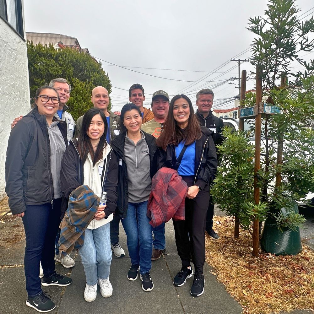 9 smiling tree care volunteers stand by a newly planted street tree.