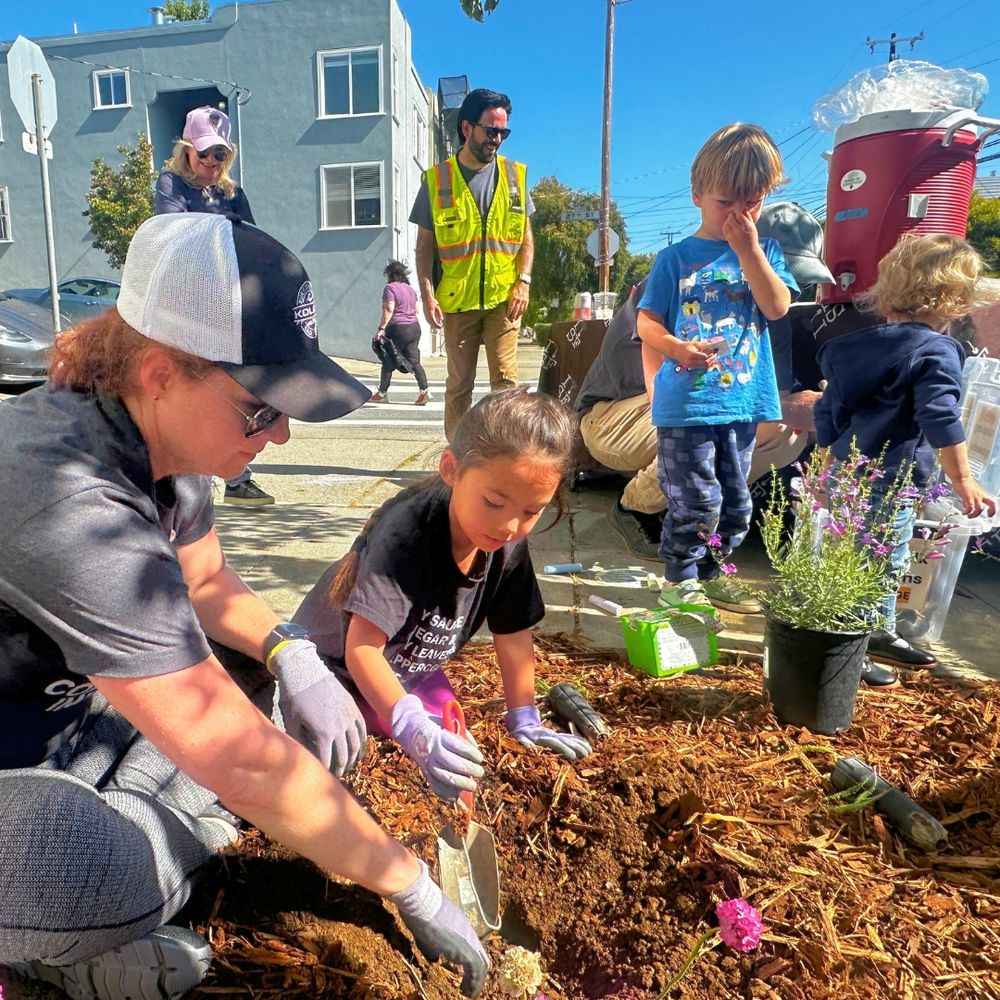 A child with an adult uses a trowel to dig a hole for a plant.
