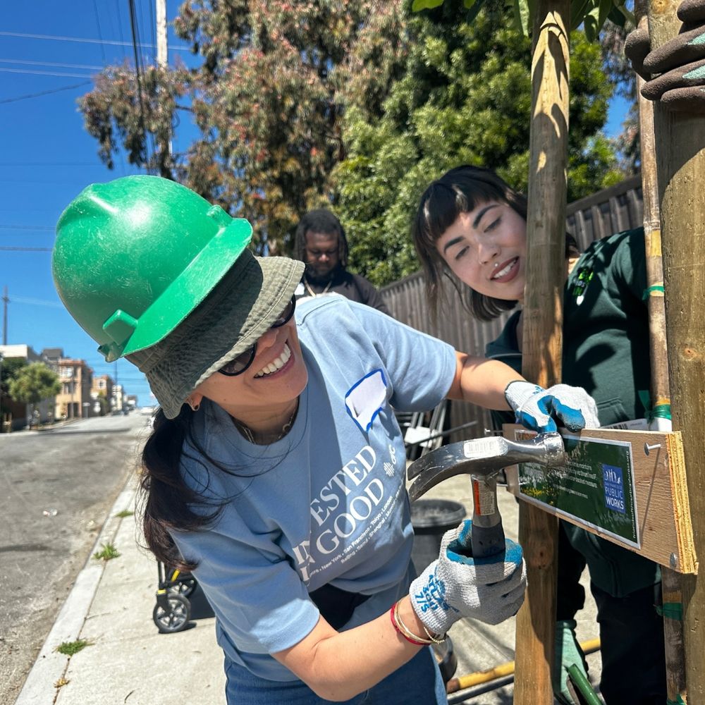 A smiling person attaches a cross brace to a stake.