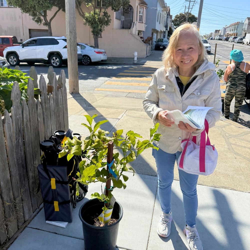 Smiling recipient of a lemon tree next to their tree.