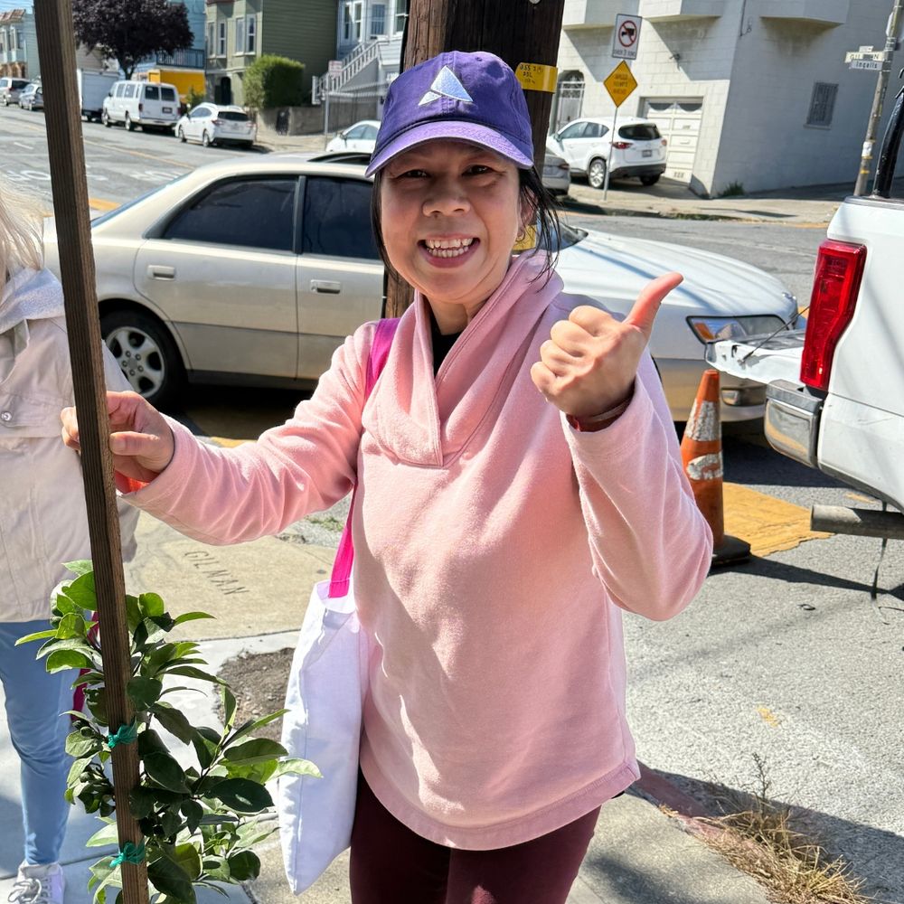 Smiling recipient of a lemon tree next to their tree.