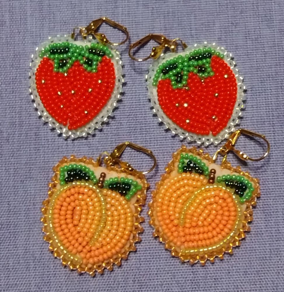 Two pairs of beaded earrings on a light purple background. One is a pair of strawberries with a white background and border and one is a pair of peaches with a neutral background and peach beaded border. 