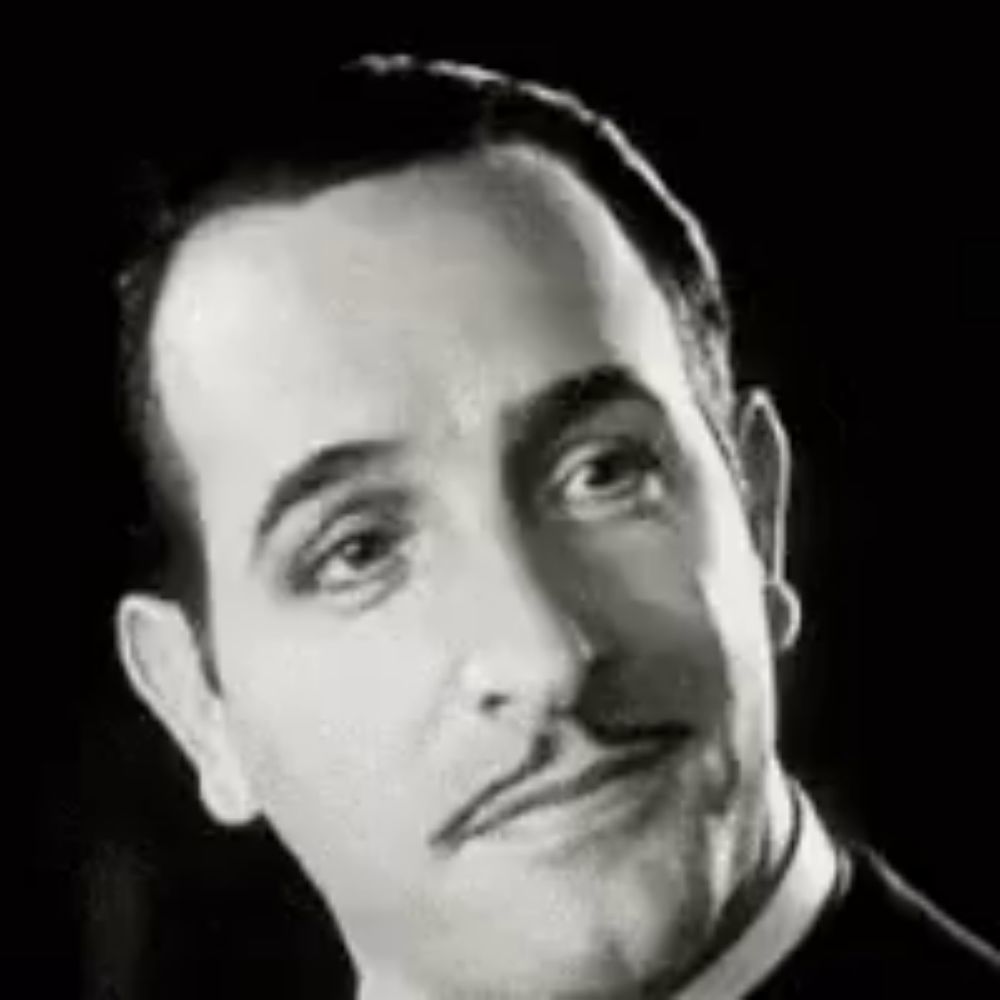 a black and white photo of a man with a mustache wearing a tuxedo and collared shirt .