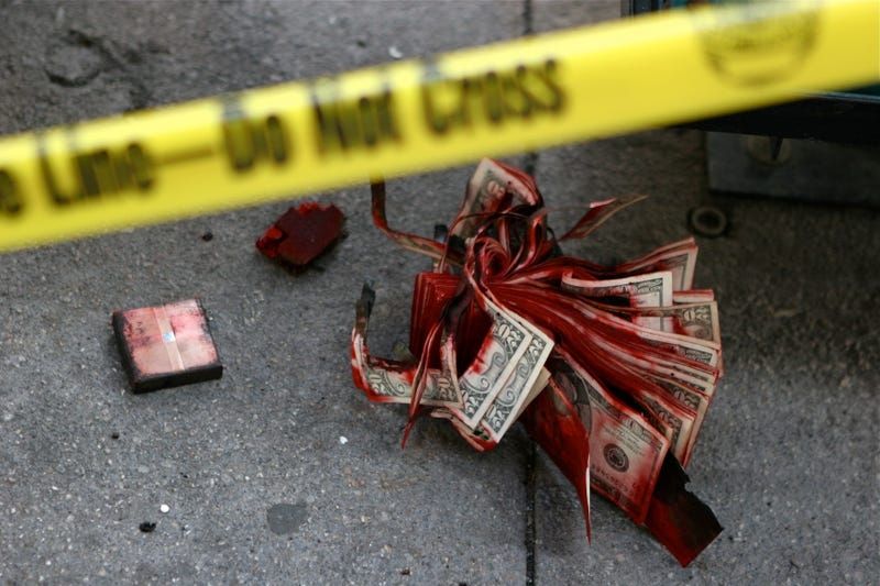 Red colored dye on a stack of money on the sidewalk.