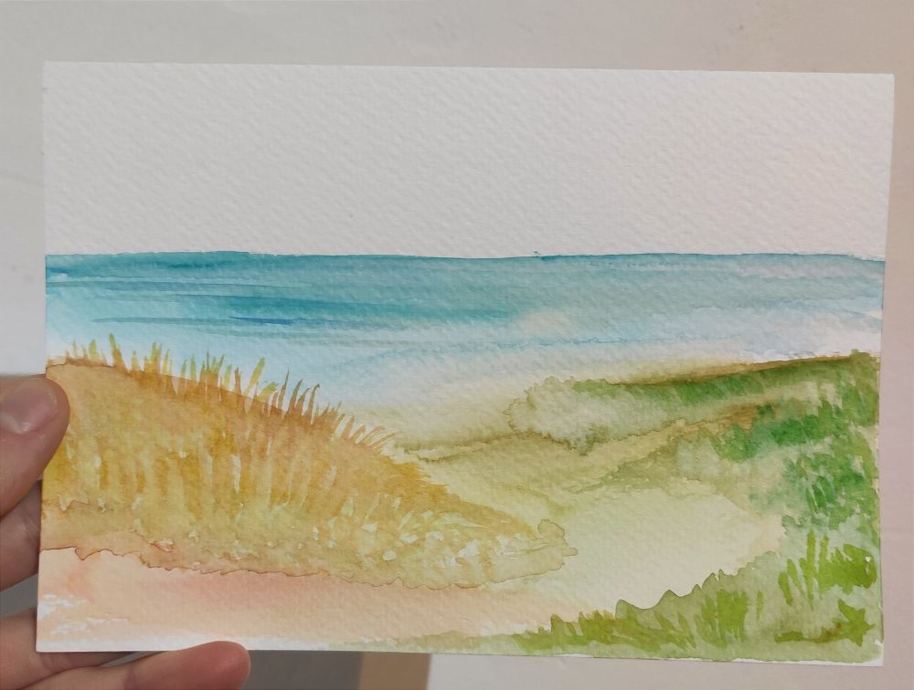 links gelb Orange Düne mit Orangem Gras, rechts flachere Düne mit grünem Gras, Meer im Hintergrund in Türkis Blau