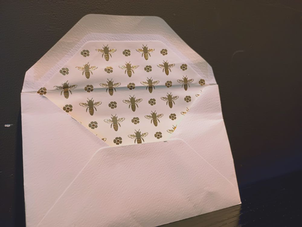 envelope with the flap open to show gold bees printed on the inside 