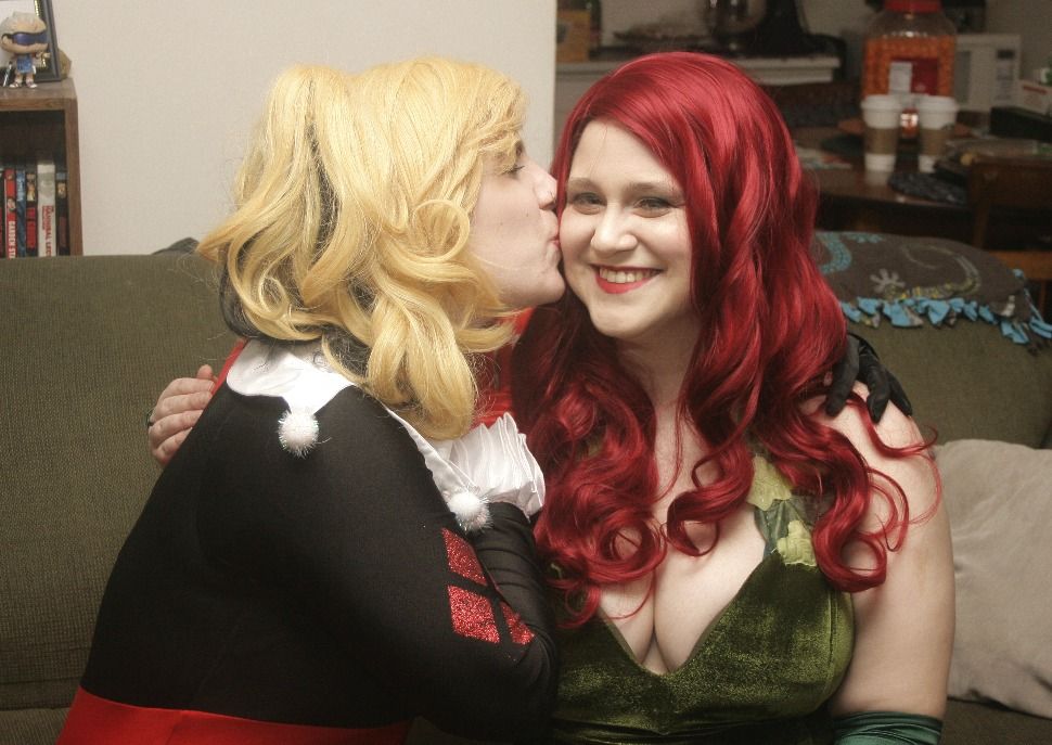Harley and Ivy cosplayers. Harley kisses Ivy on the cheek. 