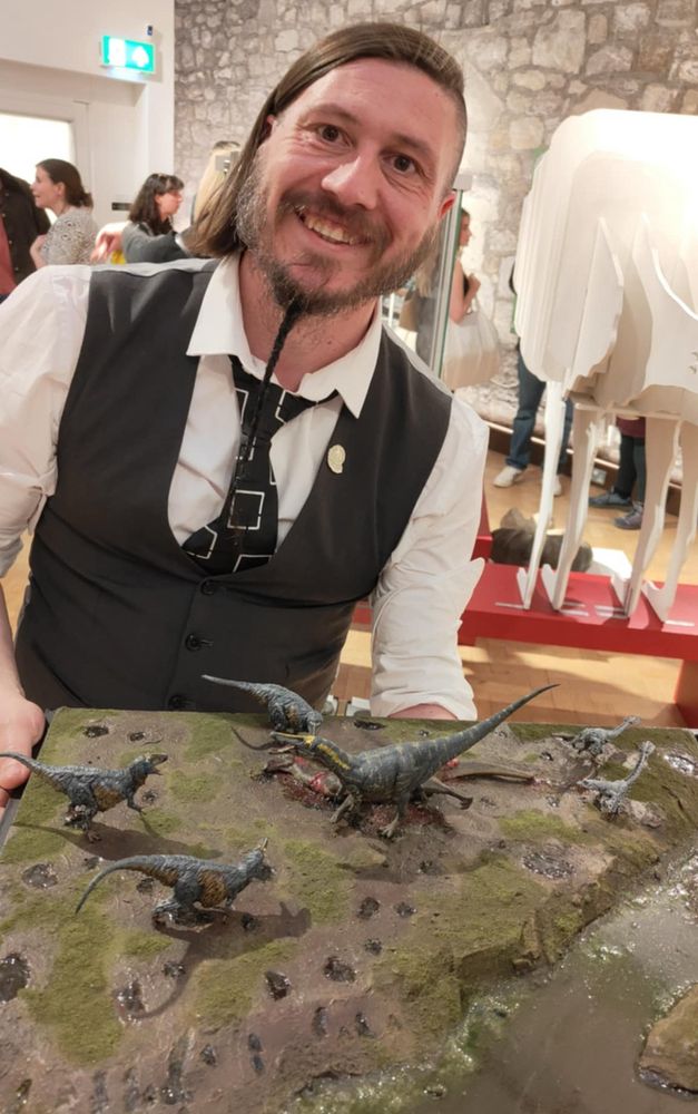 Smiling rogue, braided of beard, jaunty of angle, holding up a display of Dinosaurs 