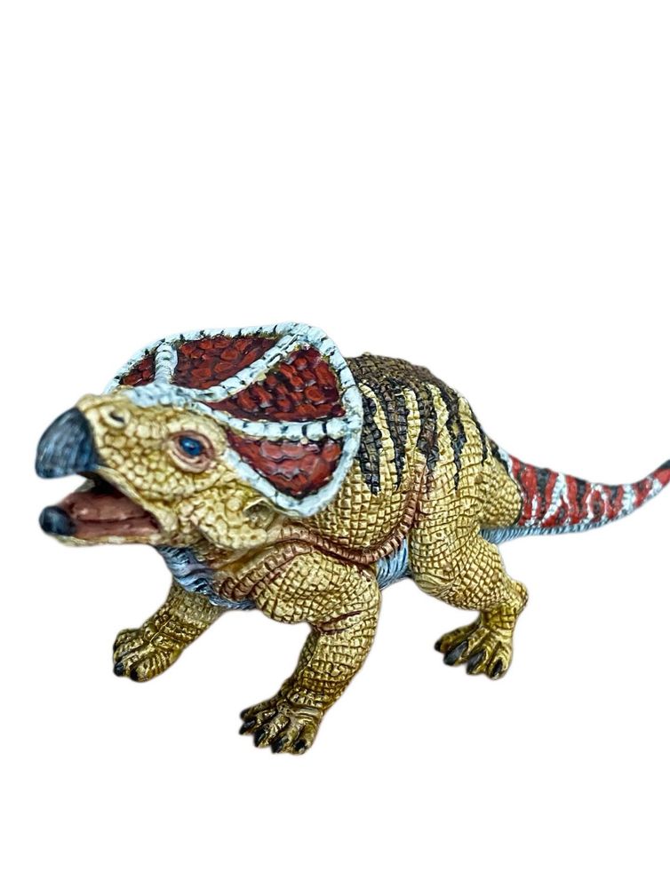 Ochre, white, red, black and brown patterned Dinosaur toy. The body is chunky, the scales tabular, the noggin is huge. The beak is sharp, the tail and head share the sane colours for signalling and it’s been a joy to paint so far  