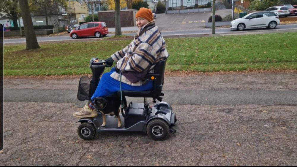 Person with beanie on wrapped up warm, and zooming happily on mobility scooter with pug.