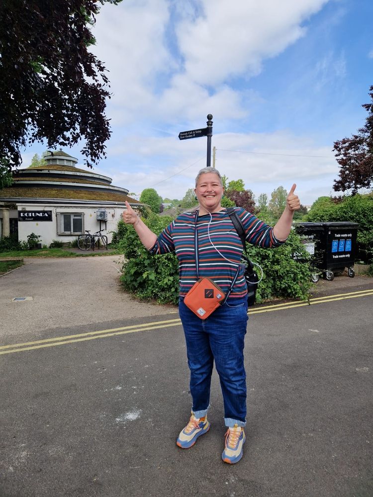 Person in stripy t shirt with ambulatory oxygen through nasal cannula, outside sunny park, two thumbs up and smiling 