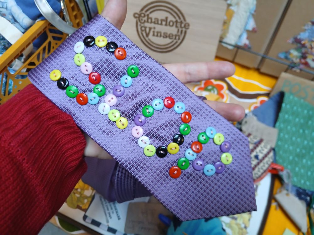 Purple tue with buttons hand sewn on that spell SLOP