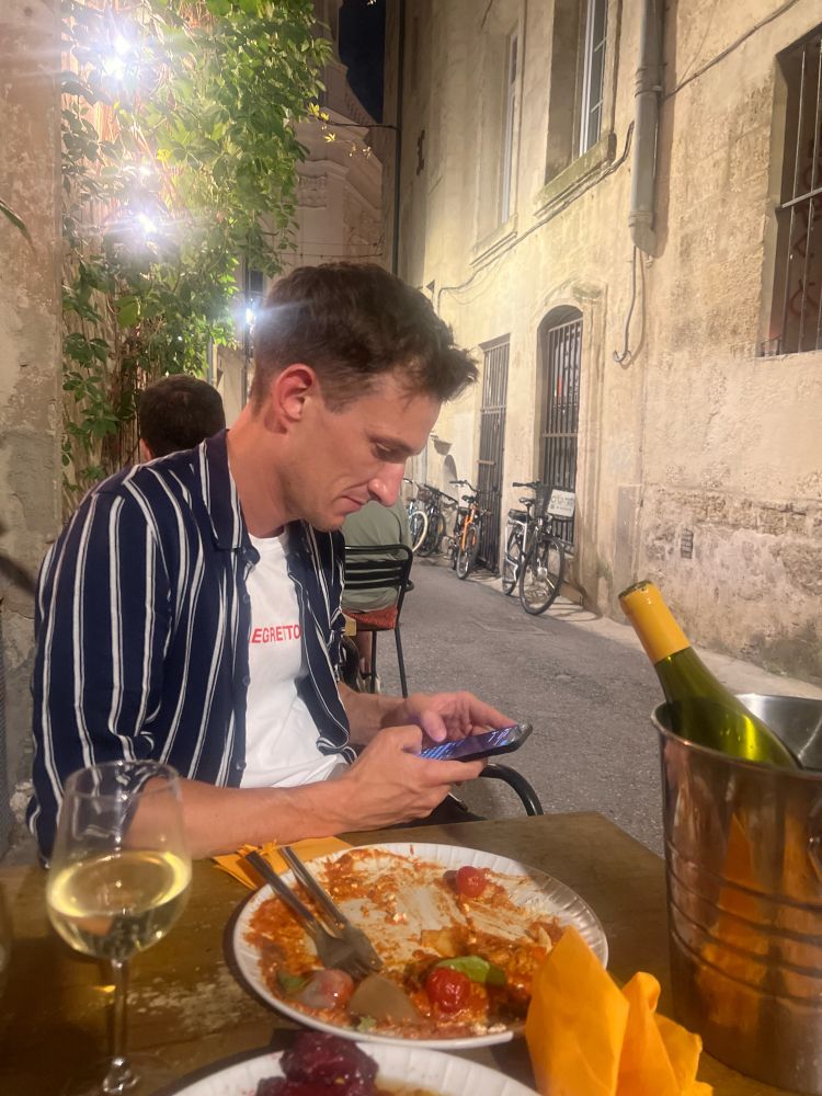 An angry man typing into his phone, sitting in a beautiful alfresco restaurant, his meal
unfinished in front of him. A second empty bottle of wine is in the bucket before him.