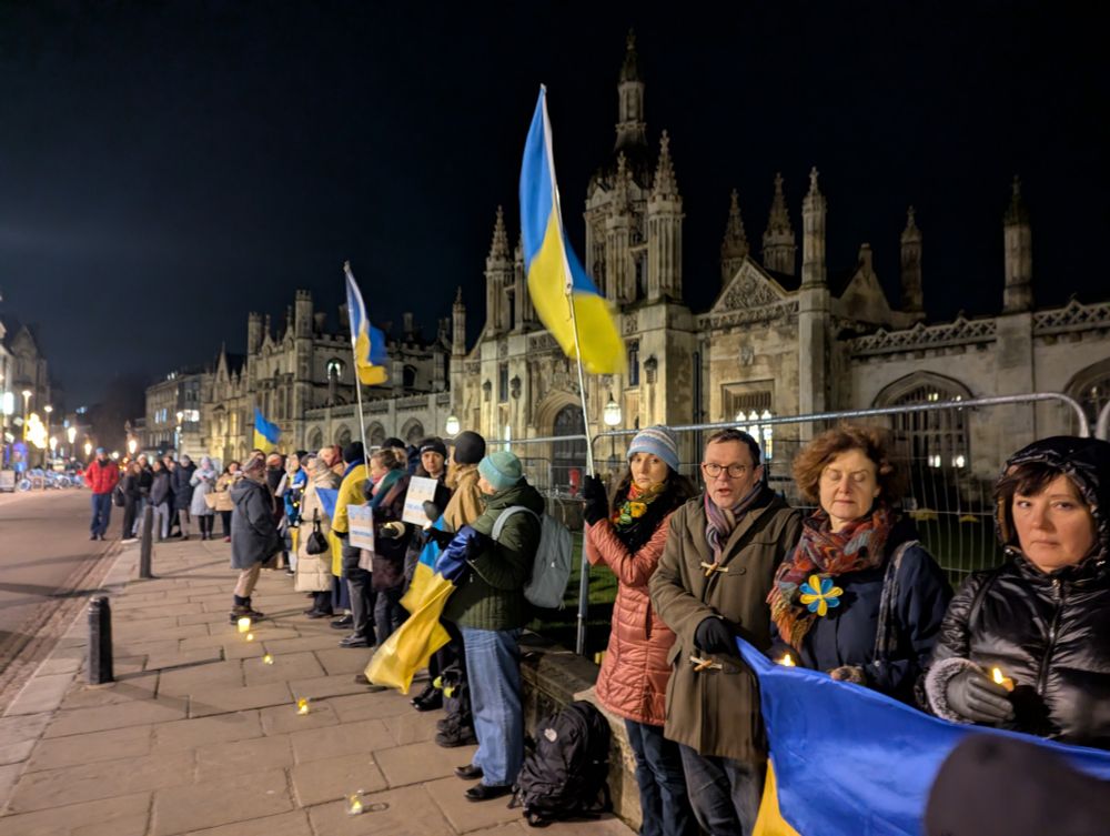 A group of people with Ukraine flags and candles in the dark on King's Parade, Cambridge 