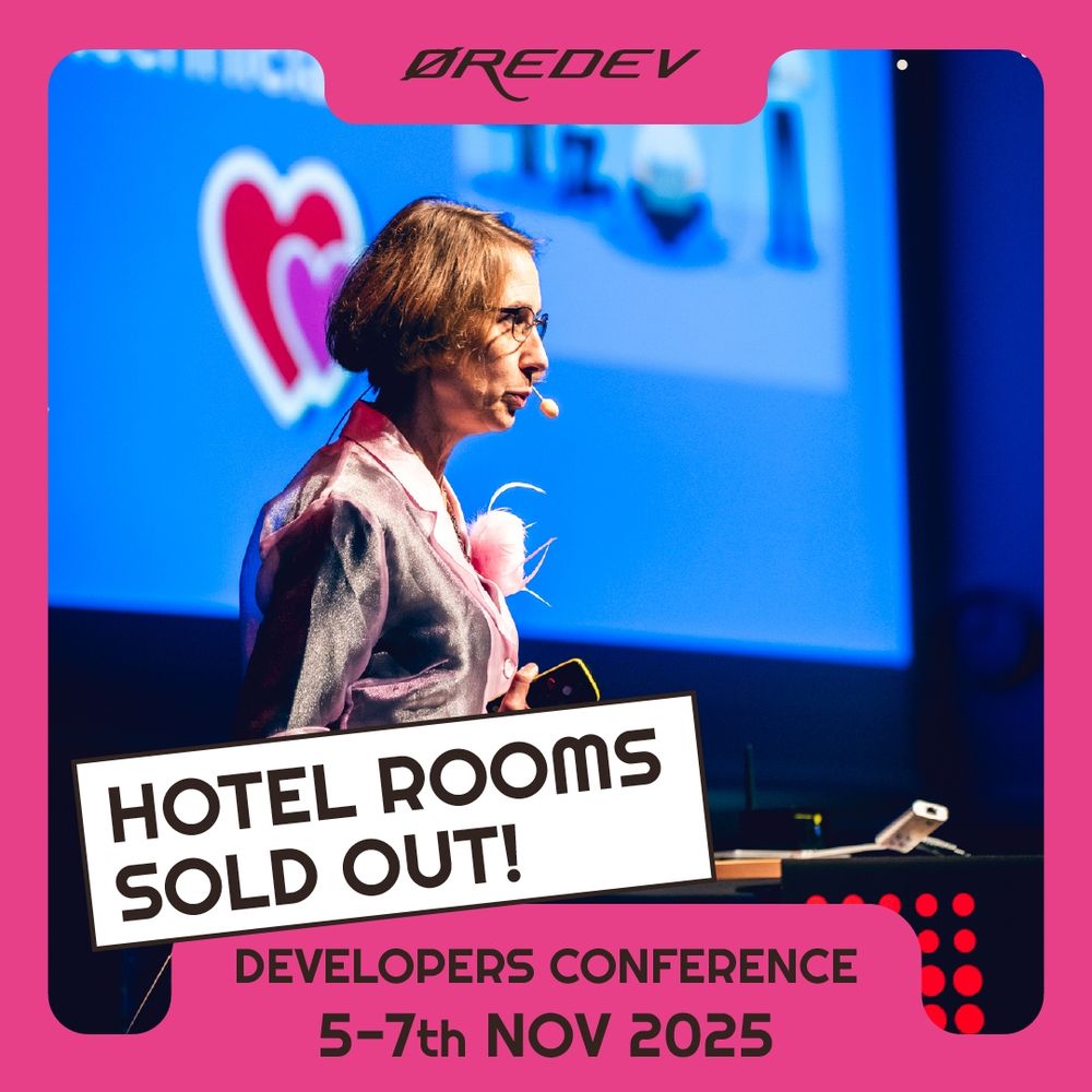 Speaker in a shiny pink jacket presenting at Øredev conference with a heart graphic on the blue screen behind them, and the text "Hotel rooms sold out"