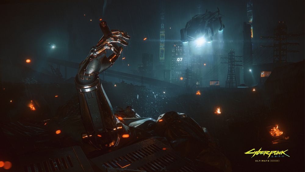 A cybernetic hand sticks out of a scrap heap within a massive junkyard. Its silver-and-orange chrome fingers hold a lit cigar. Burning fires around the junkyard create glowing patches of orange. The Night City skyline in the distance is interrupted by an AV flying through it and shining a bright white light. In the bottom right corner is the Cyberpunk 2077: Ultimate Edition logo.