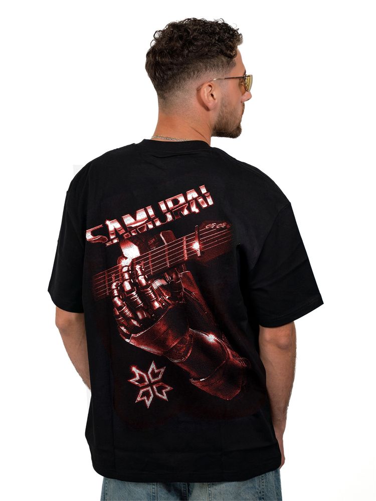 A model shows off the back of a black t-shirt, which features a large faded red-and-white graphic of the cybernetic hand of Johnny Silverhand wrapped around a guitar neck. Above the image is the word “Samurai” in all caps.