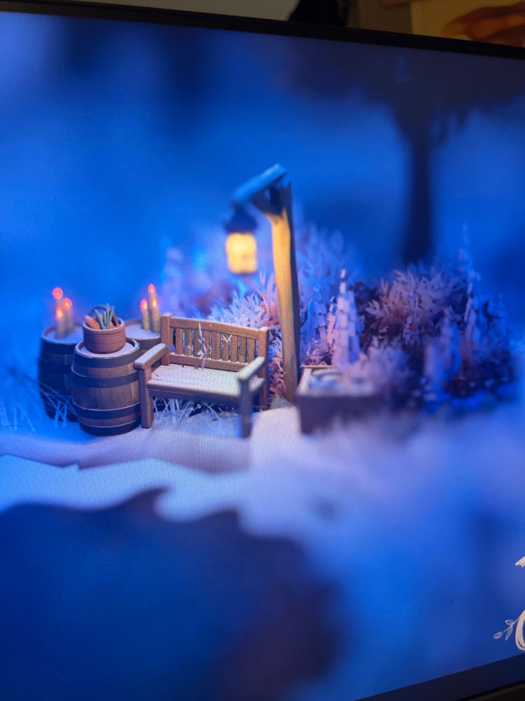 A bench under a lamp with barrels, in a snowy landscape by a frozen pond. Blue hues and rustic feel. 