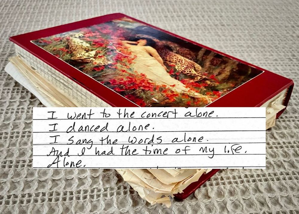 A maroon hardcover journal with an image of a woman lounging by red flowers. Pages of the journal are yellowed with age. An excerpt of the journal says: "I went to the concert alone. I danced alone. I sang the words alone. And I had the time of my life. Alone." 

(The concert was The Violent Femmes in Baton Rouge, Louisiana. 1985.)