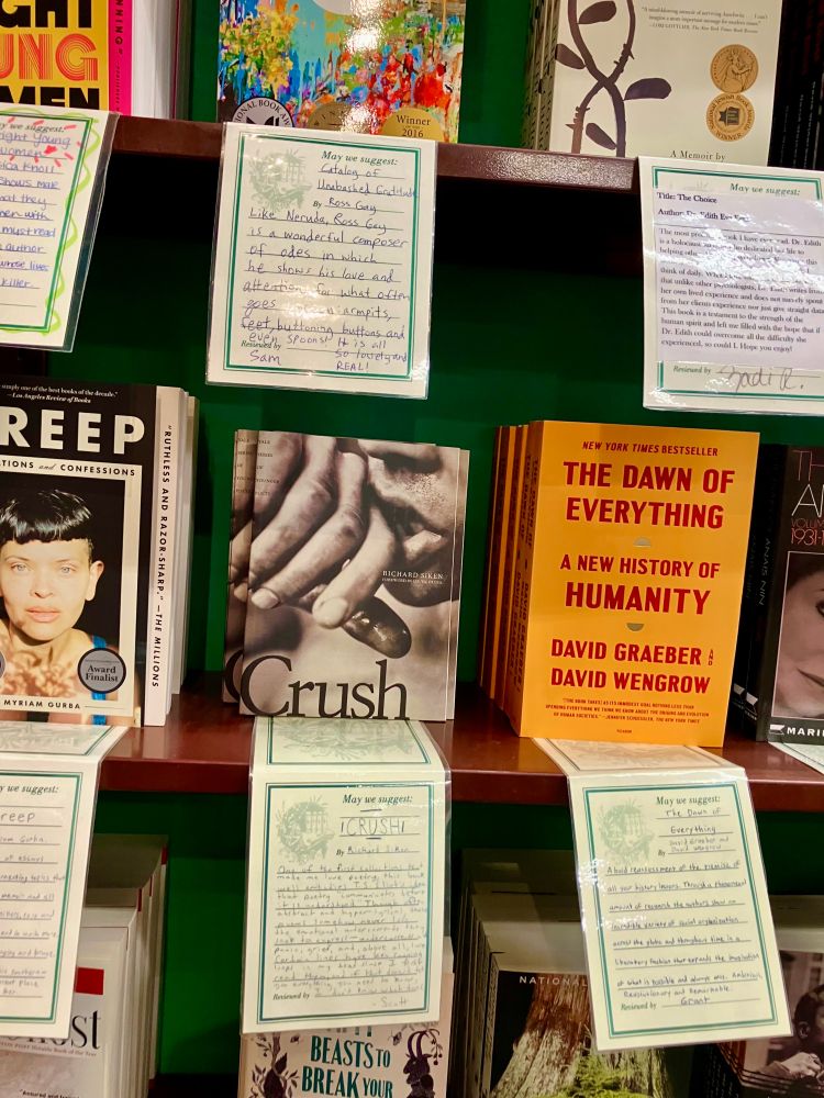 A bookstore shelf with several books. Each book has an employee review posted beneath it. CRUSH, a collection of poems, by Richard Siken is in the center of the photo.