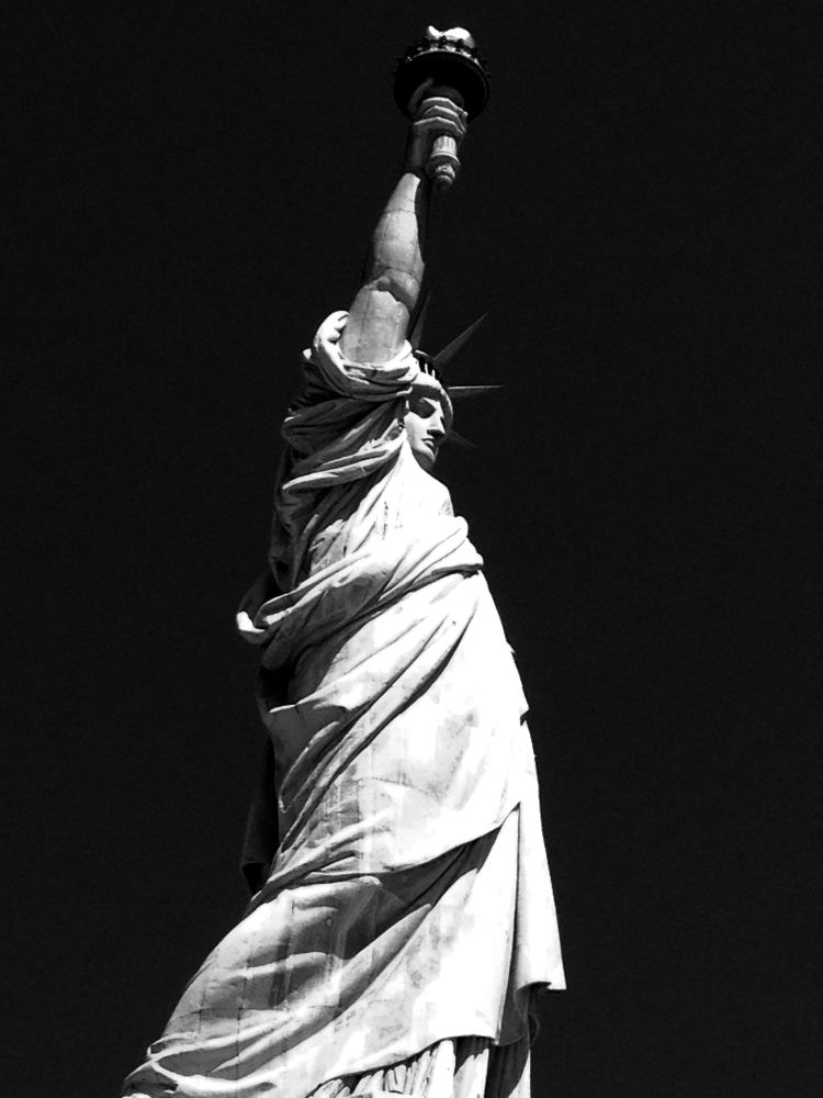 Stark black and white photograph of the Statue of Liberty. Angle up. 
