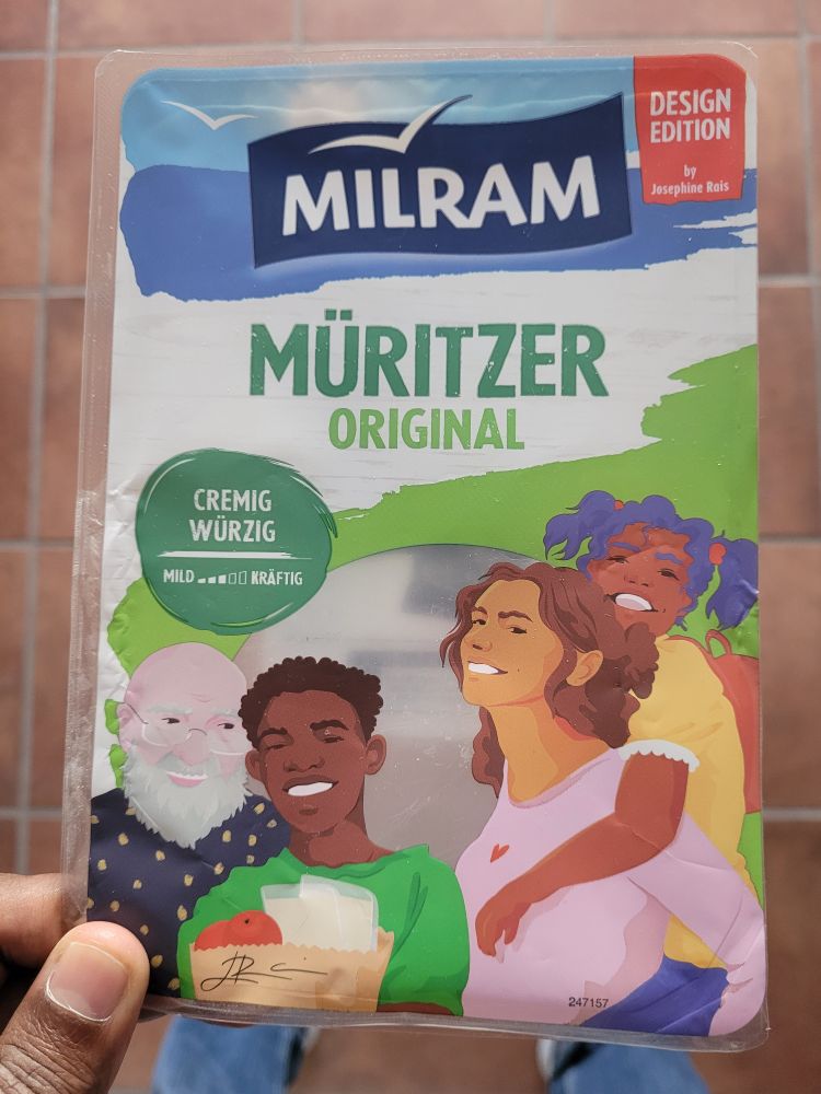 Eine leere Packung Käse von Milram in der Design Edition. Auf der Verpackung sind vier lachende Personen mit unterschiedlicher Hautfarbe zu sehen. 